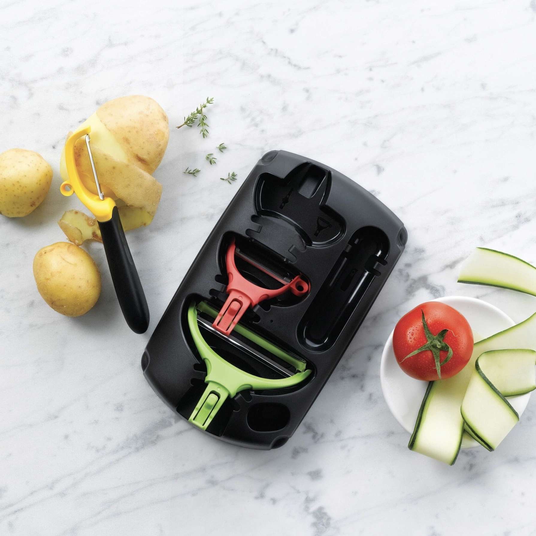Keukenhulpmiddelen set met schilmesjes en snijgereedschap voor aardappelen en courgette op marmeren achtergrond