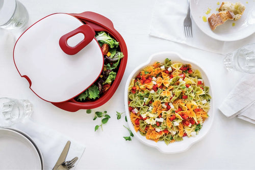 Rode saladekom met deksel en kleurrijke pasta salade op witte tafel