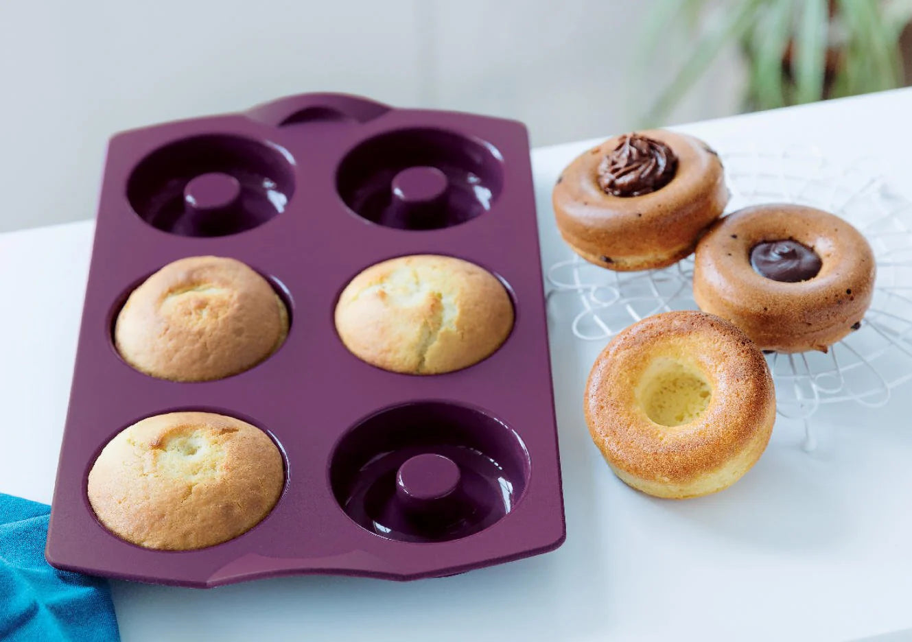 Purple silicone donut baking mold with freshly baked donuts on a white table.