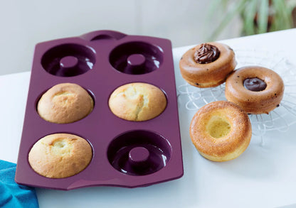 Purple silicone donut baking mold with freshly baked donuts on a white table.