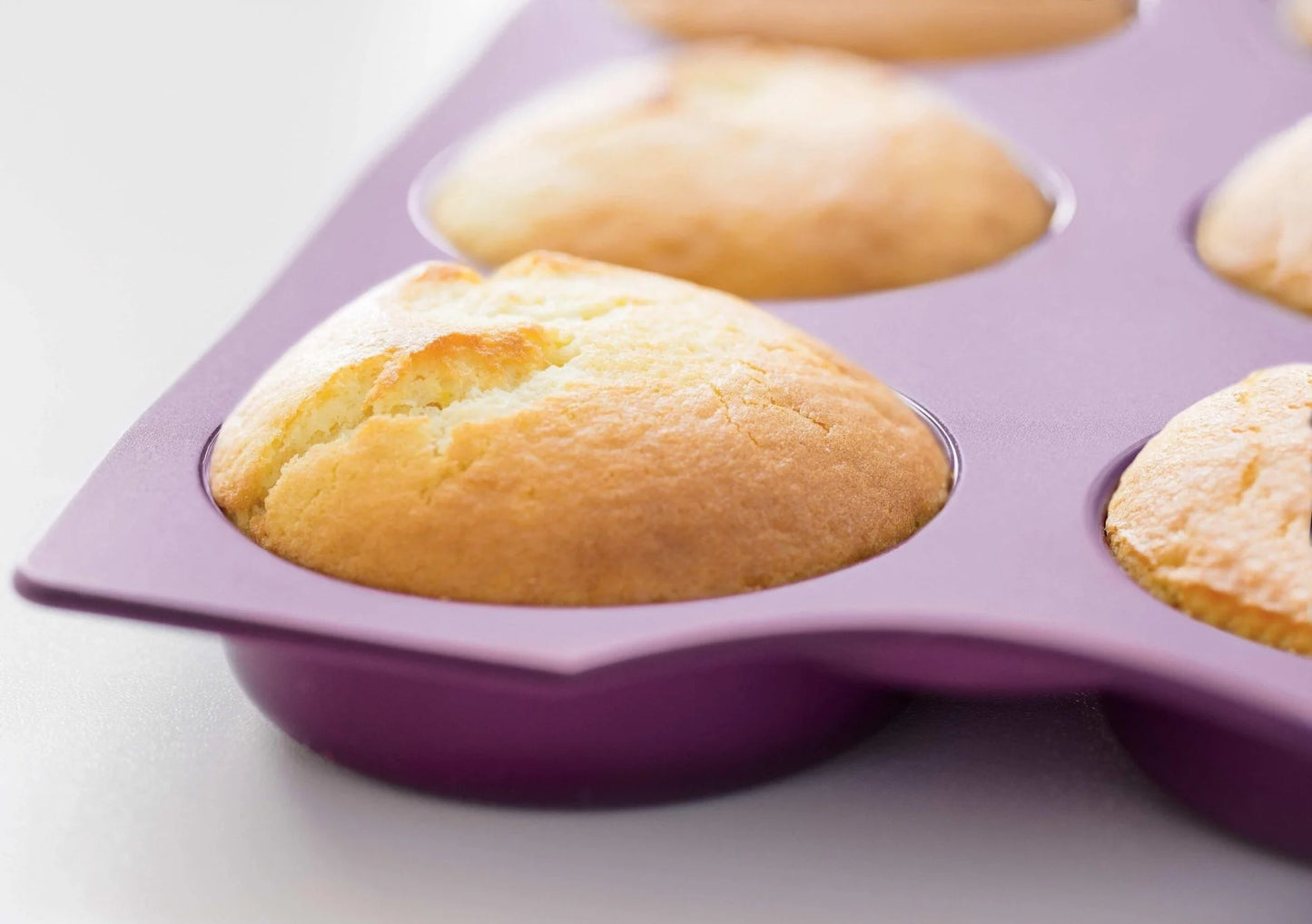 Purple silicone donut baking mold filled with freshly baked golden donuts on a light surface