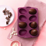 Purple silicone egg mold with chocolate eggs, plate of chocolate pieces, and marshmallows on pink background