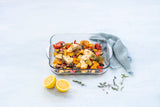 Glass baking dish with roasted vegetables, herbs and lemon on light blue background
