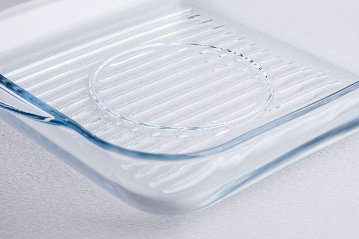 Clear glass grill baking dish with ribbed surface, close-up on light background