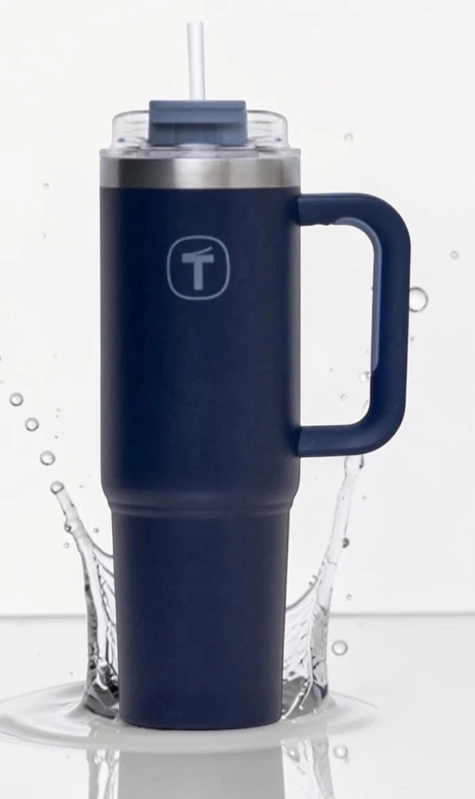 Navy blue insulated travel mug with handle, lid, and straw, standing in water splash