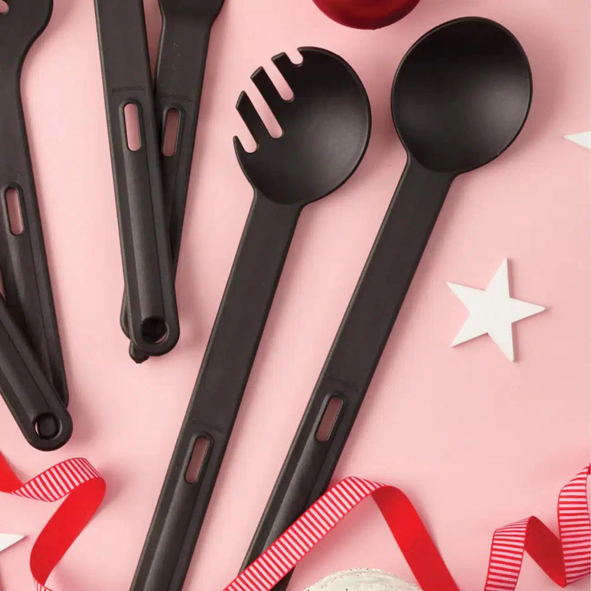 Black kitchen utensils set with spoon and spaghetti server on pink background with stars and ribbon