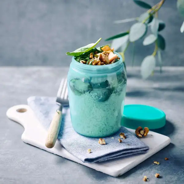 Blauwe glazen pot met groene smoothie, noten en spinazie, op marmeren bord met vork en blauw servet