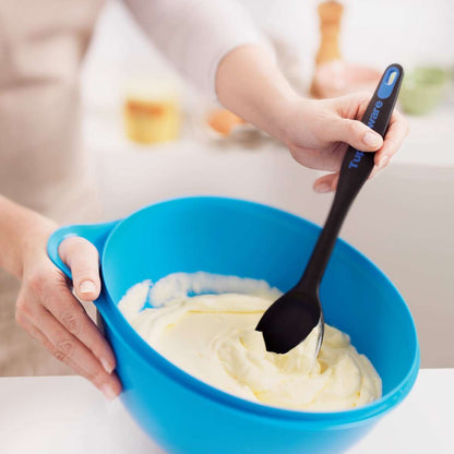 Hand mixing batter with black spatula in a blue mixing bowl on kitchen counter