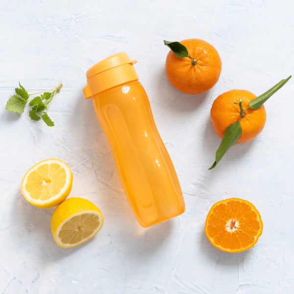 Orange Tupperware EcoFles Plus Slim 500 ml surrounded by fresh lemons and oranges.