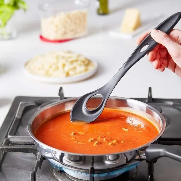 Zwarte keukenlepel roert tomatensaus in pan op gasfornuis, perfect voor culinaire avonturen