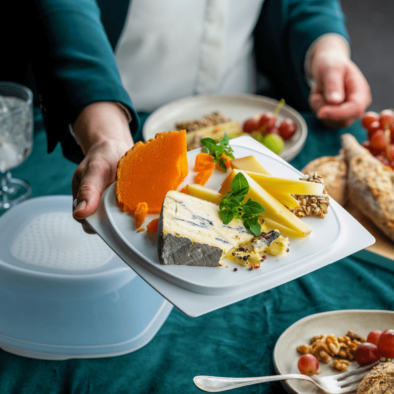 Rectangular cheese container with assorted cheeses on a plate at a dining table