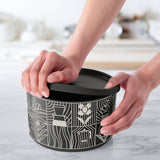 Hands opening a black kitchen container with white modern graphic designs on a marble countertop