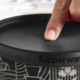 A finger pressing the airtight seal on a black Tupperware coffee and cookie container lid.