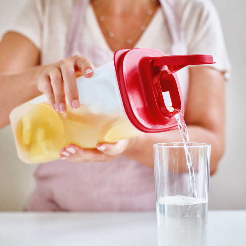 Person pouring water from a Tupperware square fridge jug into a glass.