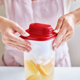 Hands closing the red lid of a Tupperware 2L square fridge pitcher filled with lemon water and ice.