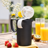 Zwarte melkopschuimer met wit schuim op een houten tafel met fruit en sap.