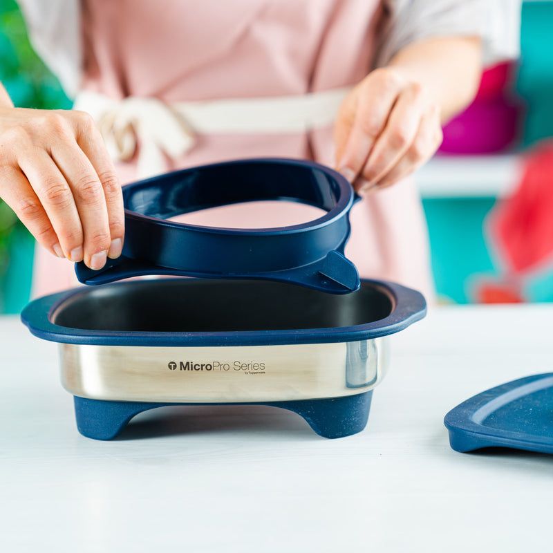 Hands placing a blue Tupperware Micro Pro Grill Ring onto a stainless steel microwave pan.