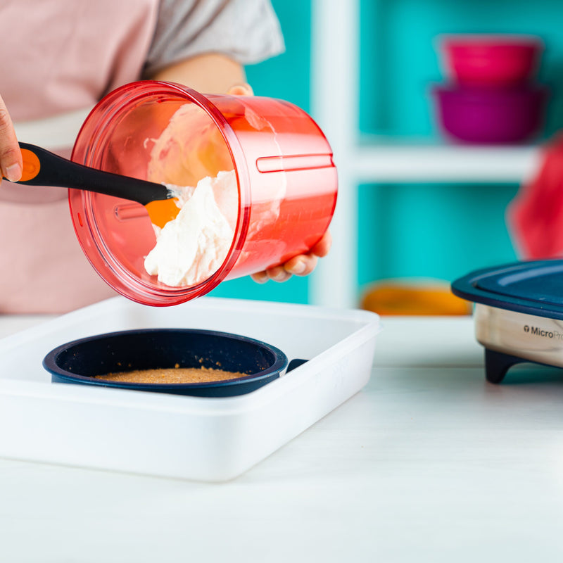 Person using a spatula to transfer cream from a red Tupperware container into a Micro Pro Grill Ring
