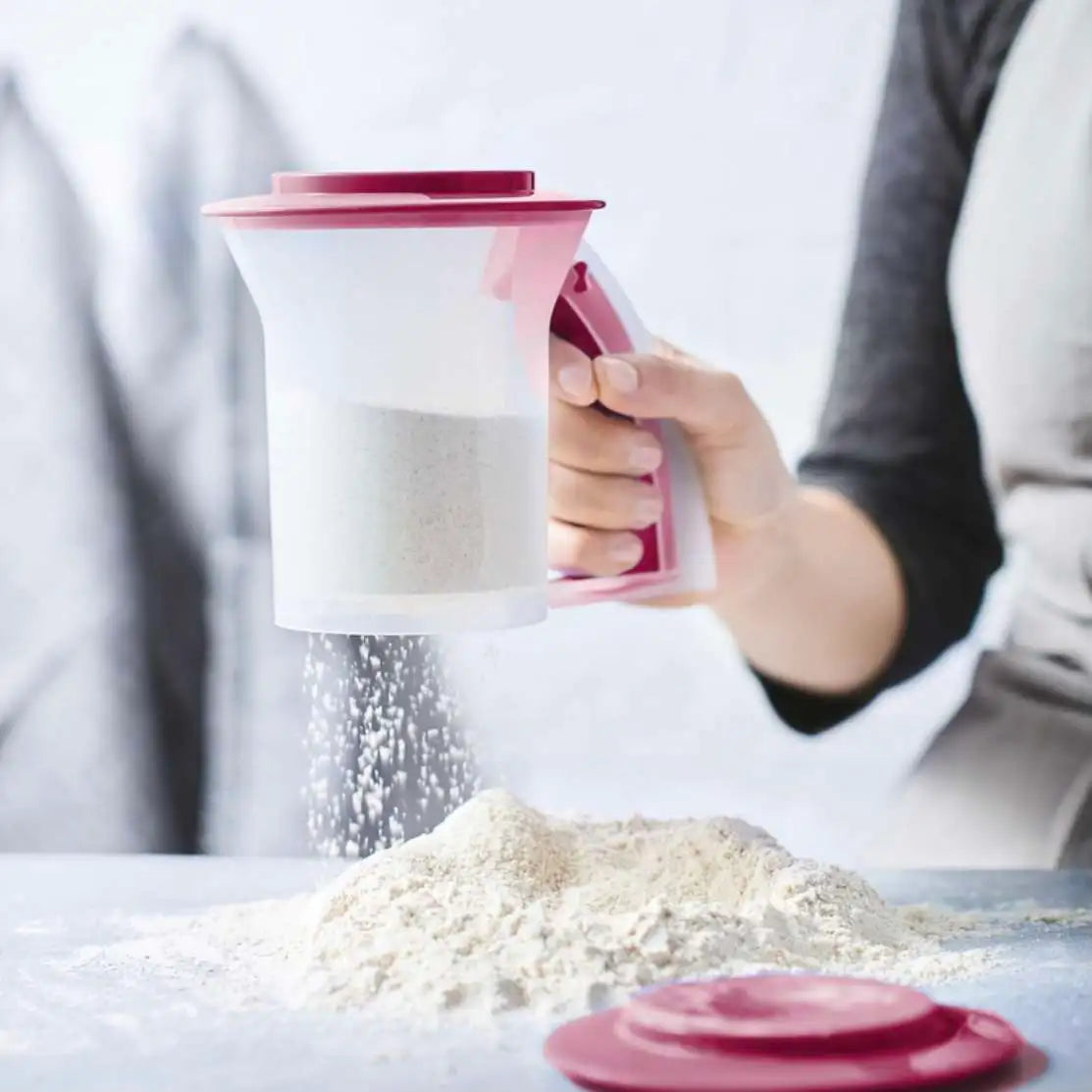 A person using a Tupperware Poeder Zeef to sift flour onto a surface.
