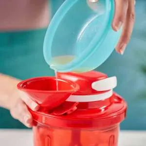 Pouring liquid into a red kitchen food processor using a funnel