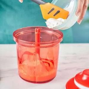 Red manual food chopper with a spatula adding cream, kitchen tool on marble surface