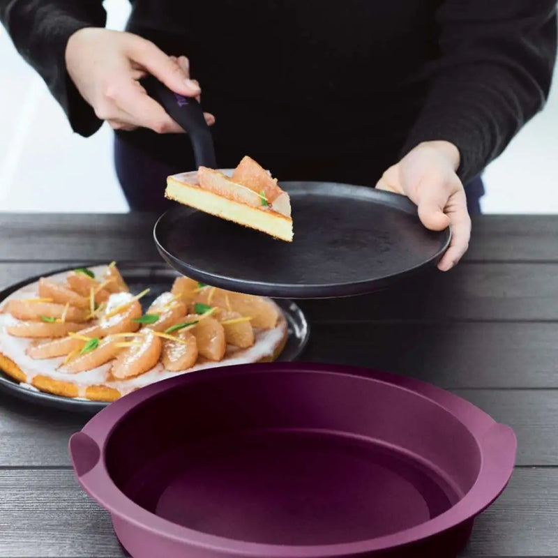 Using a Tupperware cake server to lift a slice of pear tart onto a black plate.