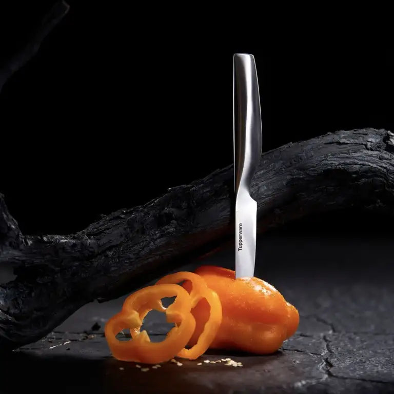 Stijlvolle Tupperware keukenmes snijdt oranje paprika op donkere achtergrond