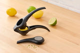 Black citrus press and zester on wooden counter with lemons and limes
